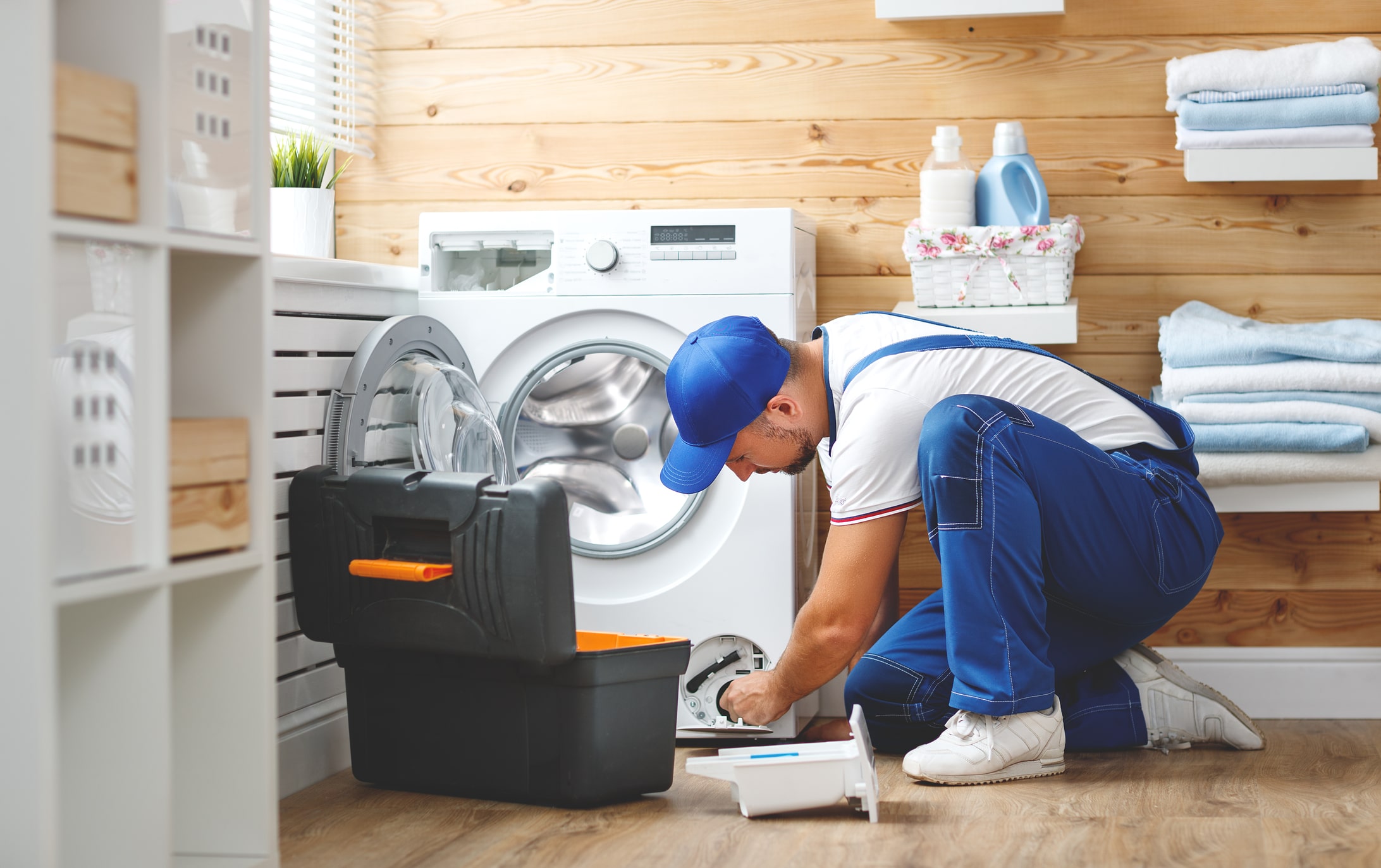 Technician repairs washing machine in laundry room.
