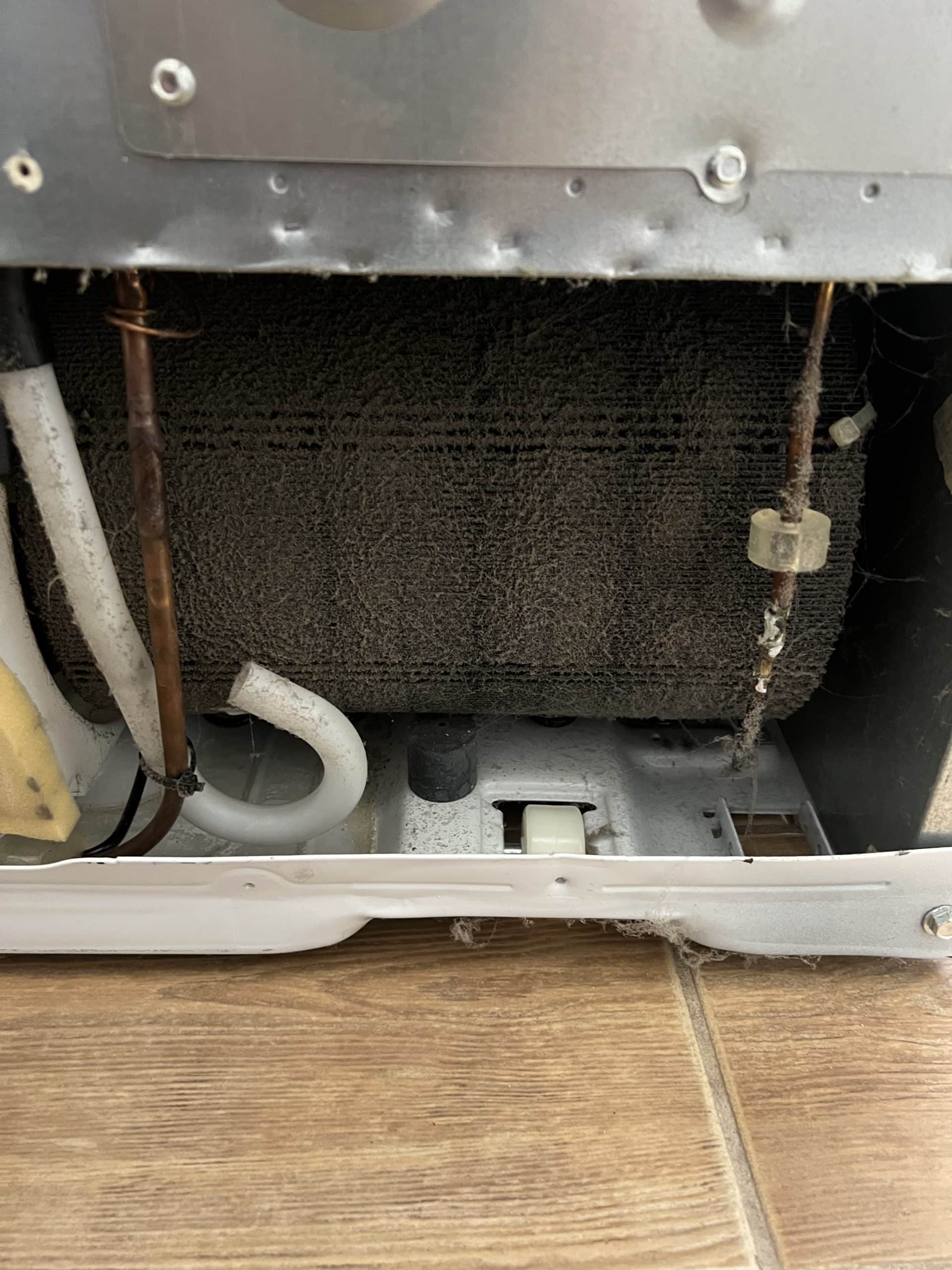 Inside view of dusty refrigerator coils and pipes.